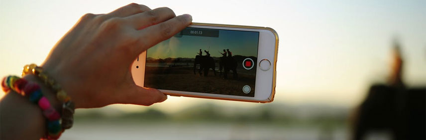 main tenant un smartphone en train de filmer une scène.